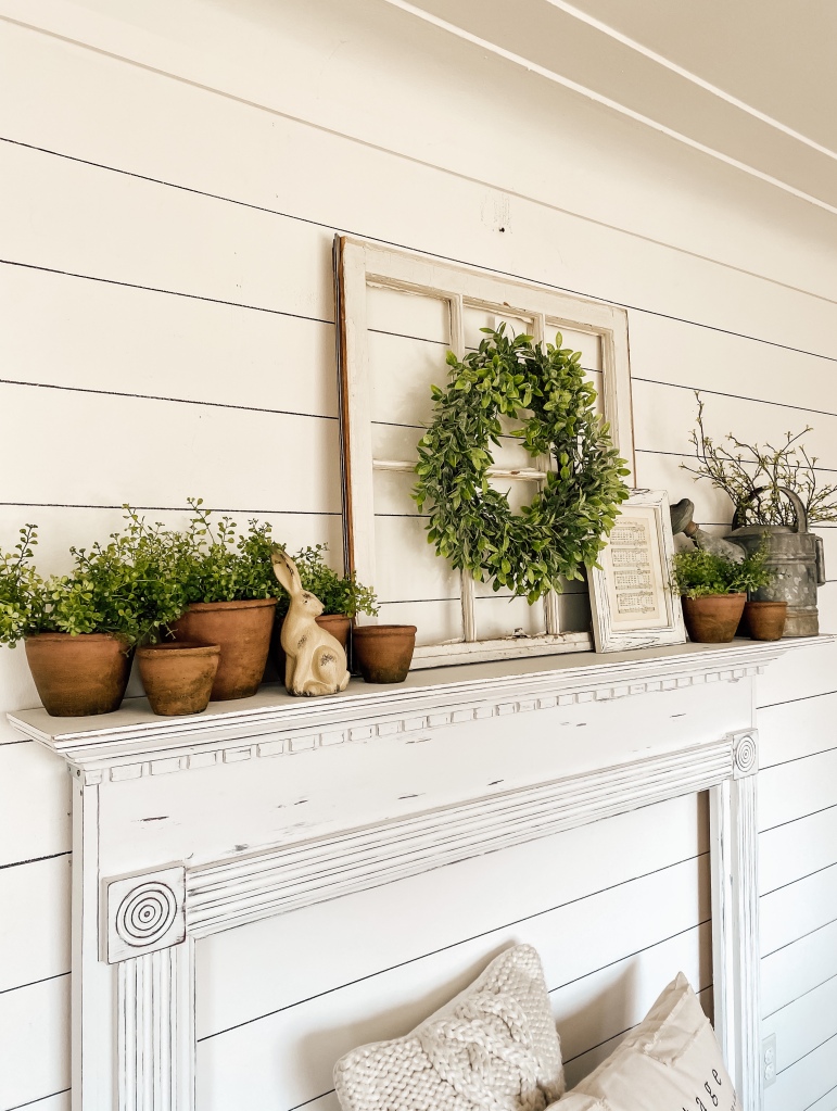 Mantel on shiplap wall decorated with old window, wreath, terra cotta pots